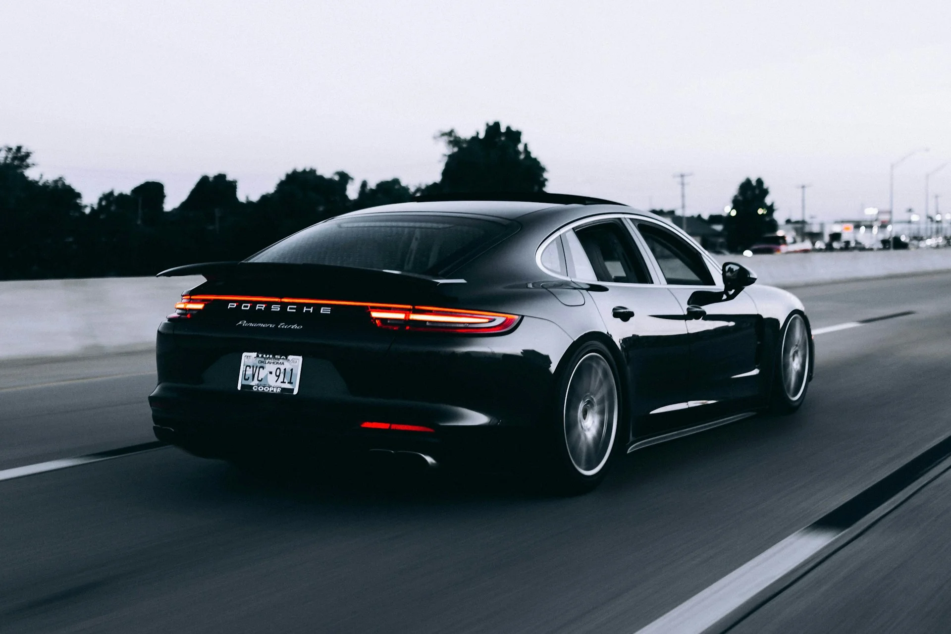 Porsche negro con reflejos sobre la carrocería y luces traseras encendidas. Fotografía de referencia.